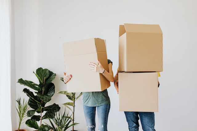 person on the left is holding one box and the person on the right is holding two with a white background behind them